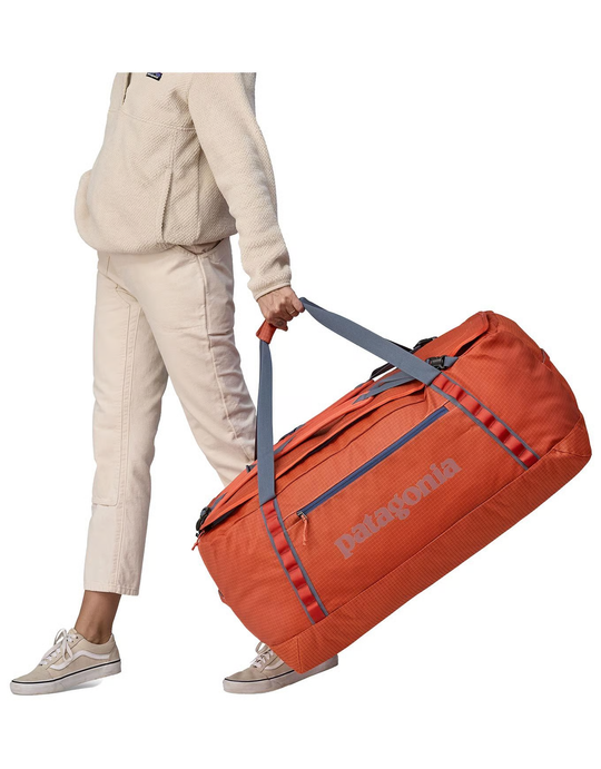 Orange Black Hole Duffel 100L held by a person, showing durable construction and carrying handles.