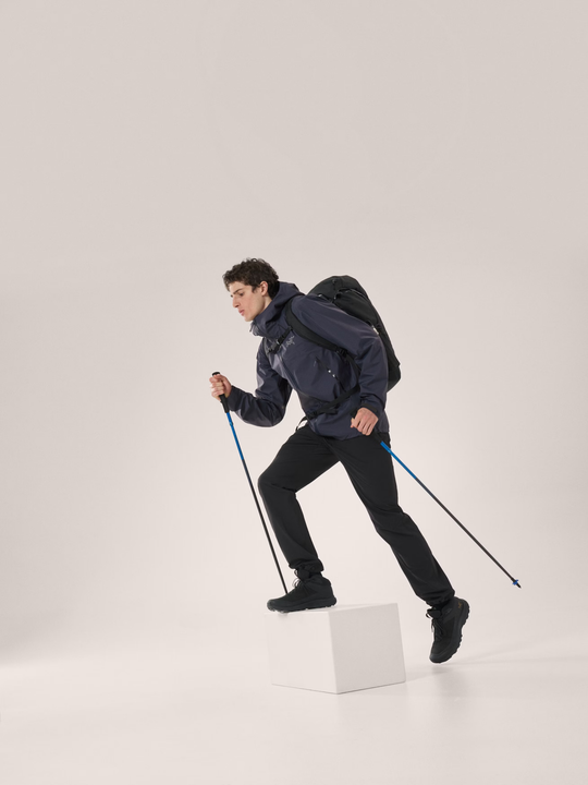Man hiking in a Beta SL Jacket with poles, showcasing waterproof and breathable lightweight outdoor gear.
