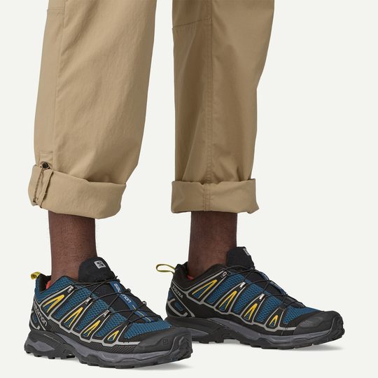 Men's Quandary Pants in beige with adjustable ankle cord, paired with blue and black hiking shoes.