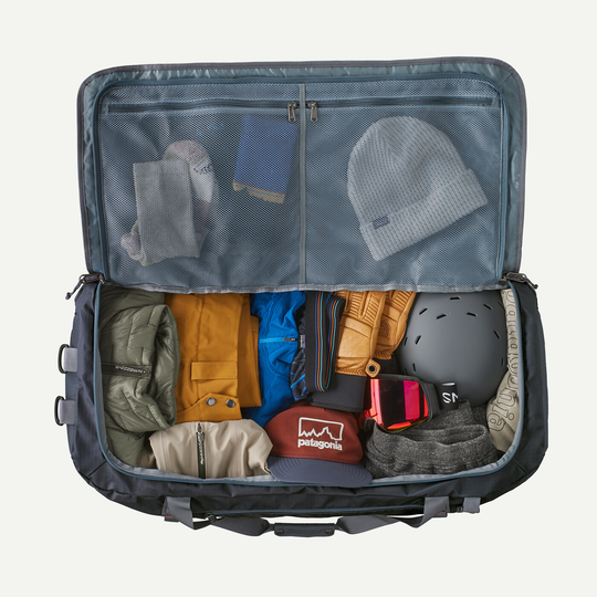 Black Hole Duffel 100L open with packed travel gear and accessories.