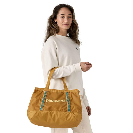 Black Hole Tote 25L in gold held by a person wearing a beige outfit.