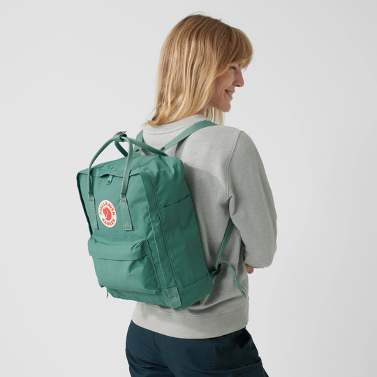 Zaino Kånken classico in tessuto Vinylon verde con logo Fjällräven, donna di profilo.