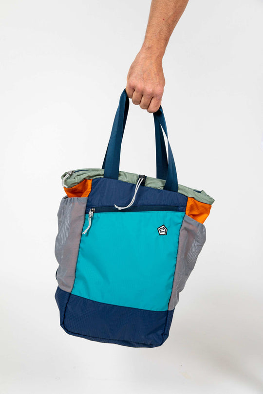 Colorful technical backpack held by a hand against a neutral background.