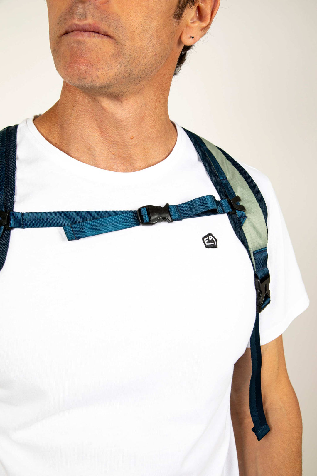 Man wearing white shirt with blue backpack straps, focusing on chest detail.