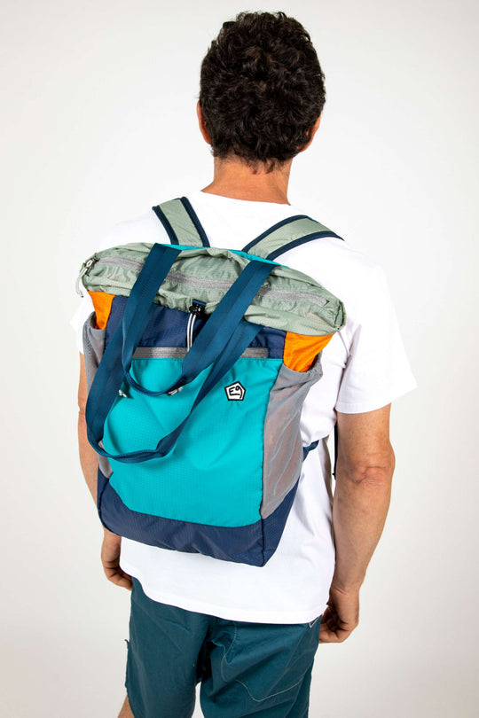 Multicolor bagpack worn by a person in a white shirt and teal shorts.