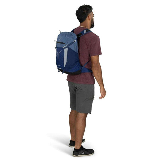 Zaino giornaliero blu in nylon, con pannello frontale elastico grigio, tasche laterali e spallacci imbottiti.
