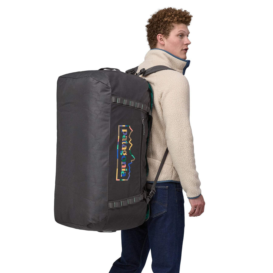 Man carrying Black Hole Duffel 100L backpack in black, featuring recycled materials and removable straps.