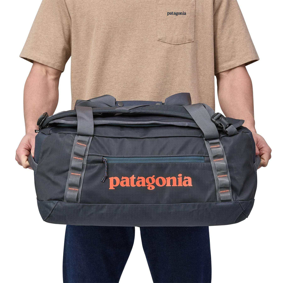 Black Hole Duffel 40L held by person, water-repellent, 100% recycled materials, ergonomic straps, compact design.